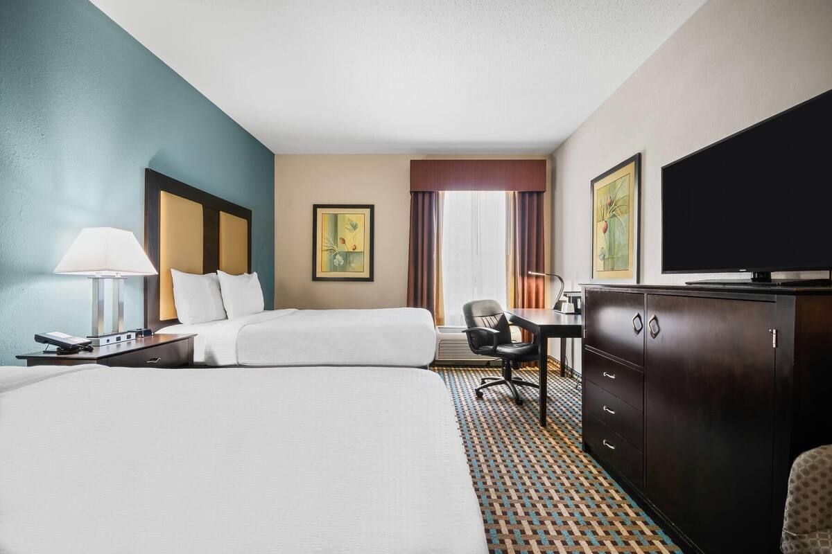 A hotel room with two beds, a desk, a chair, a TV, and a cabinet.