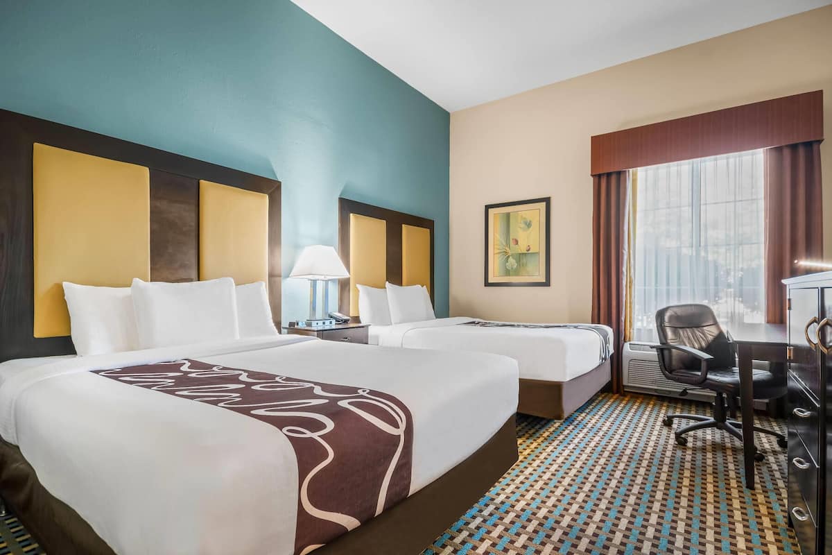 A hotel room with two beds, a desk, a chair, and a window with curtains.
