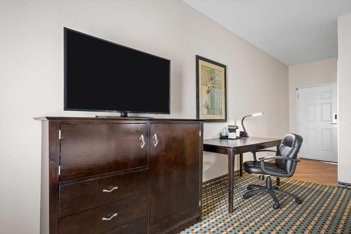 A room with a dark wooden cabinet, a flat-screen TV, a desk with a chair, and a patterned carpet.