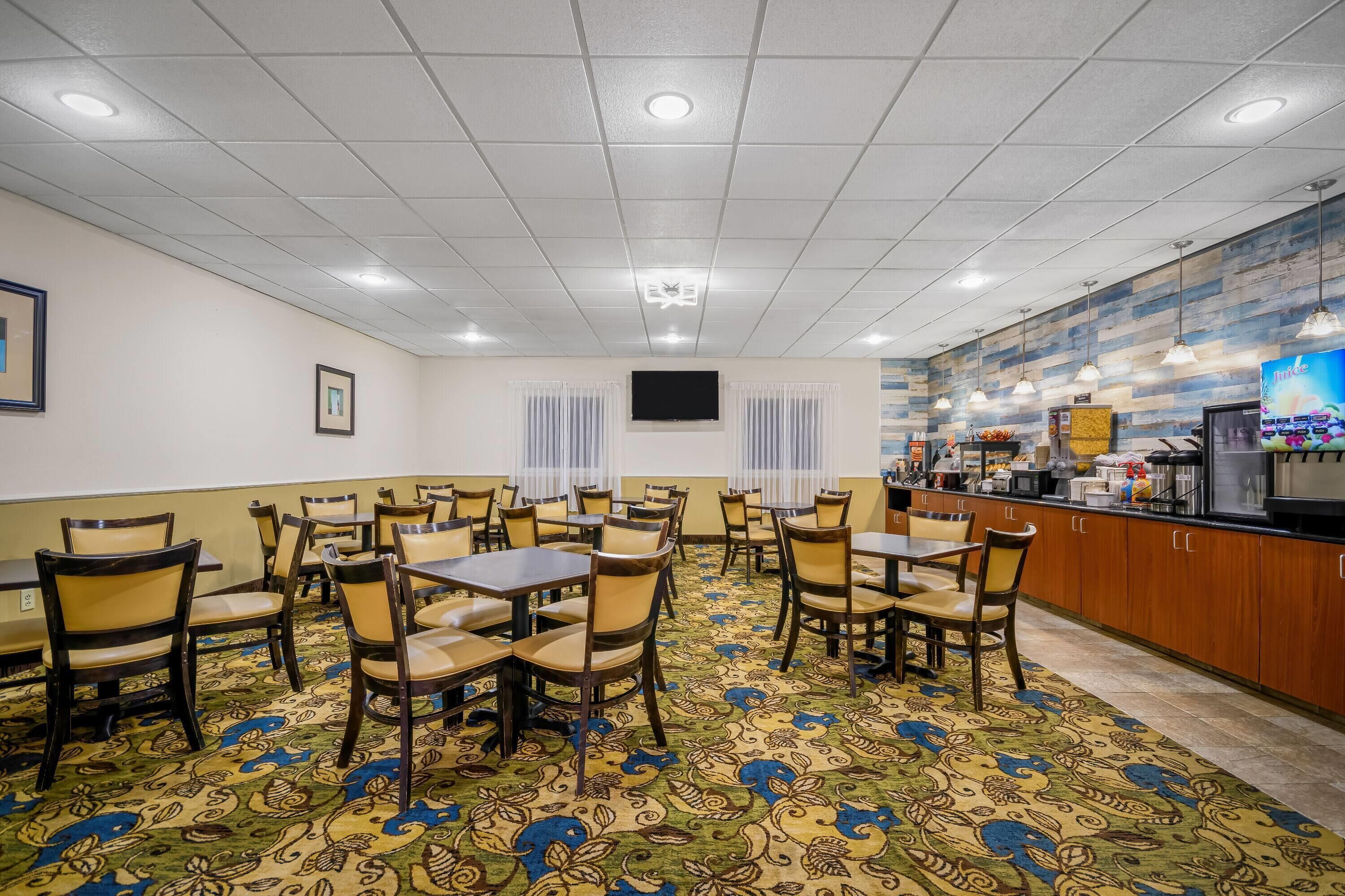 Une salle à manger d’hôtel avec des tables et des chaises, un comptoir de cuisine et un tapis à motifs.