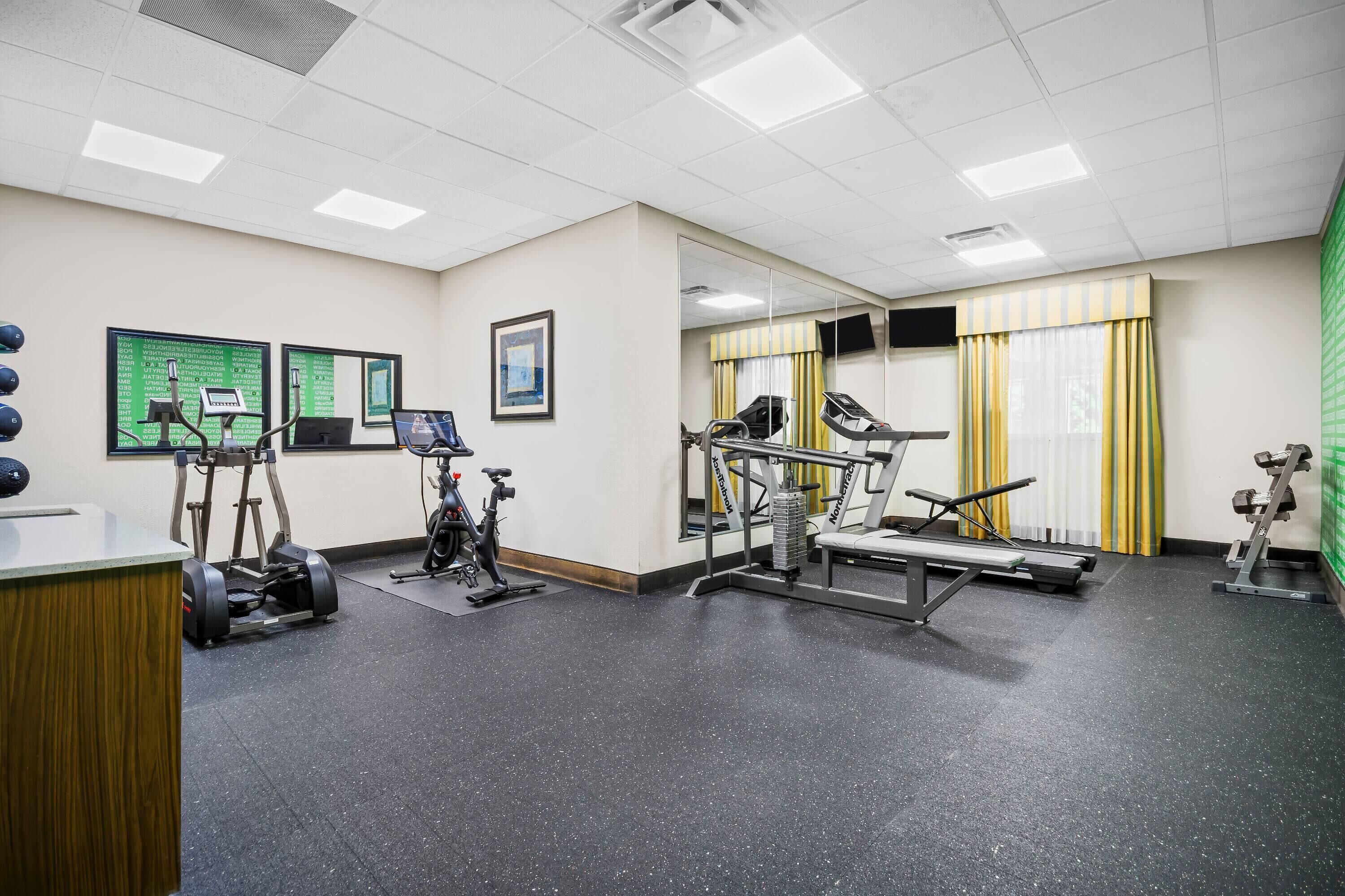 A gym with exercise equipment, a mirror, and a green screen.