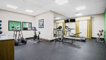 A gym with exercise equipment, a mirror, and a green screen.