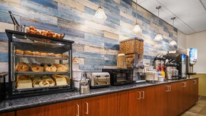Una barra de desayuno con una variedad de pasteles, una máquina de café y un tostador.