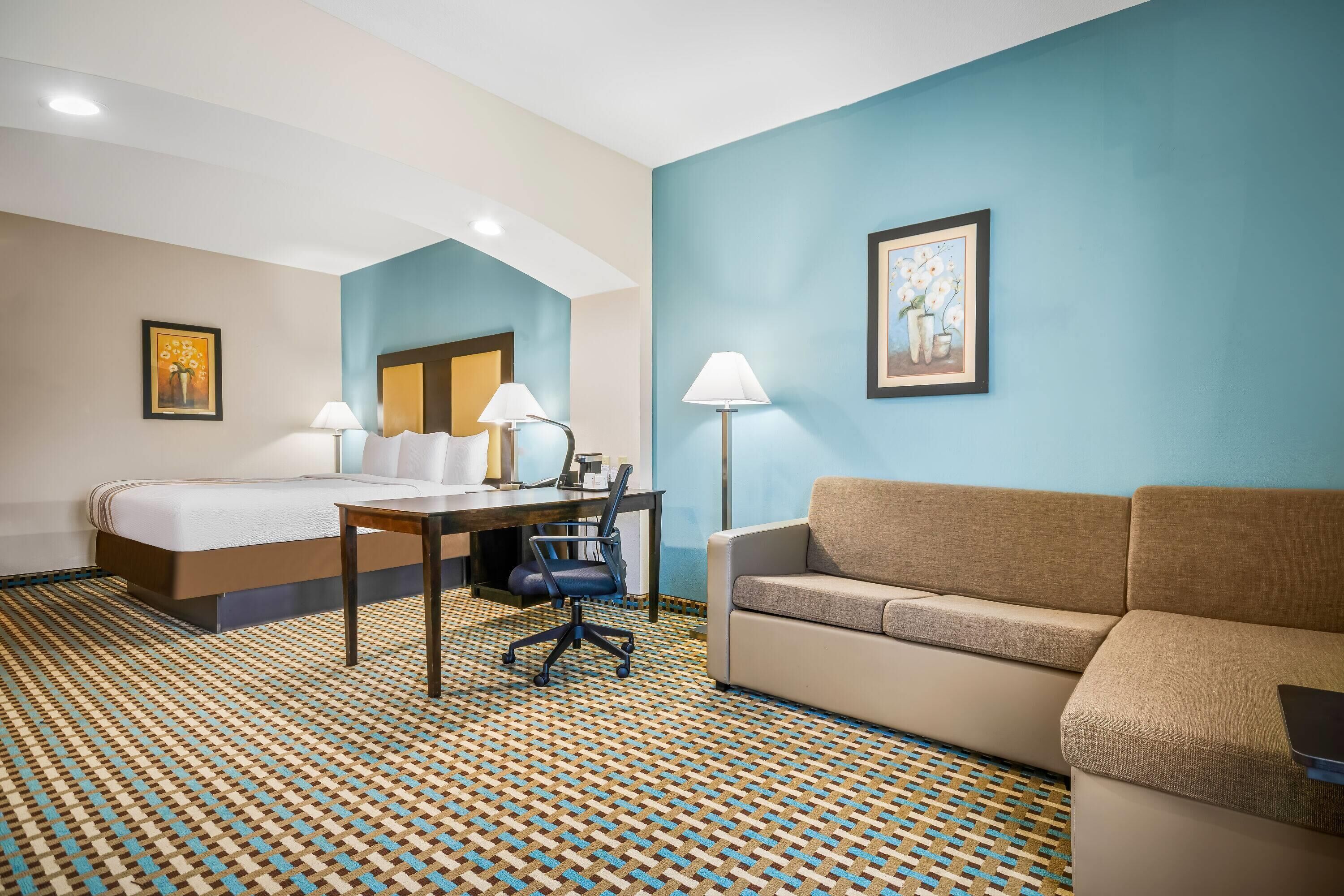 A hotel room with a bed, a desk with two lamps, a sofa, and a patterned carpet.
