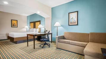 A hotel room with a bed, a desk with two lamps, a sofa, and a patterned carpet.