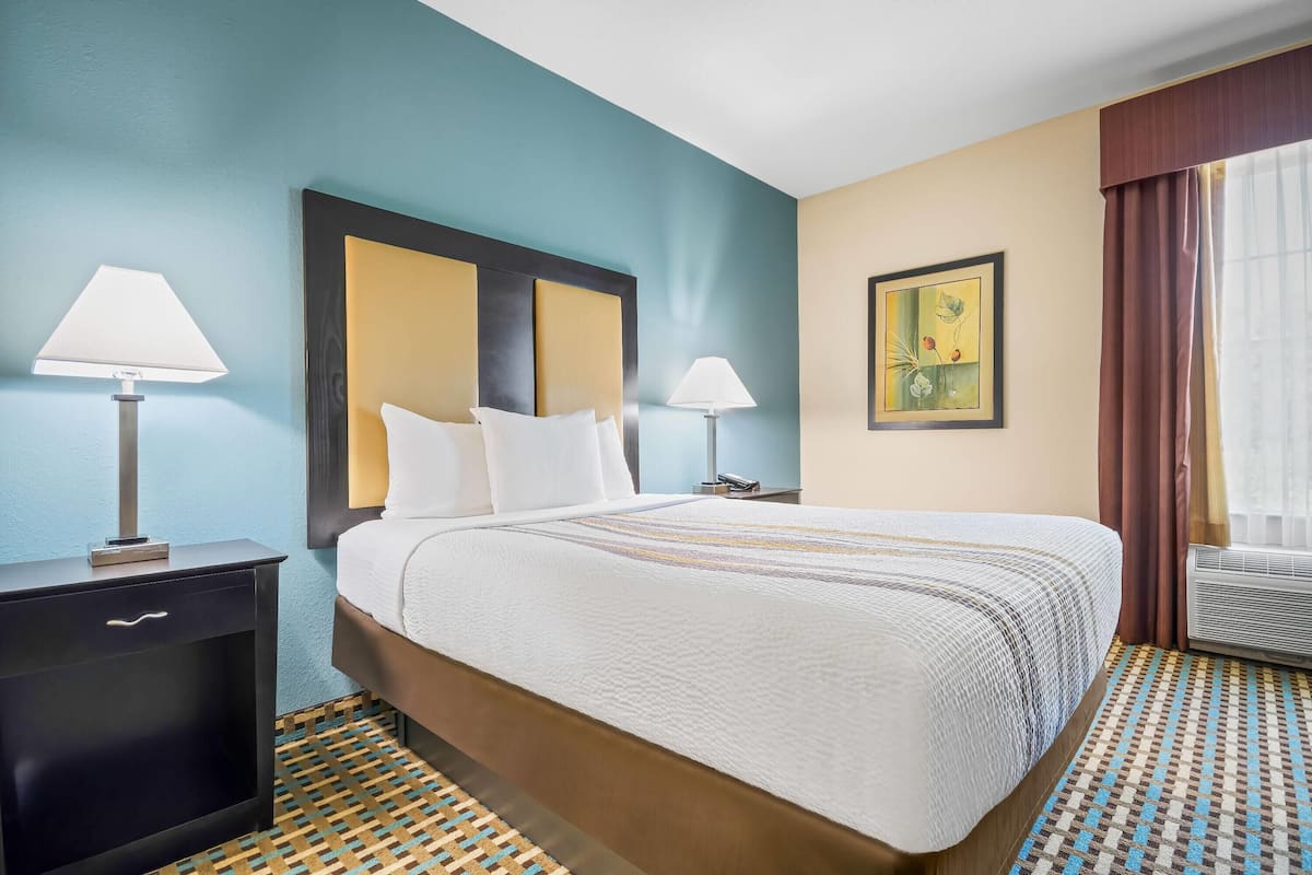 A hotel room with a bed, two bedside tables, a lamp on each table, a patterned floor, and a painting on the wall.