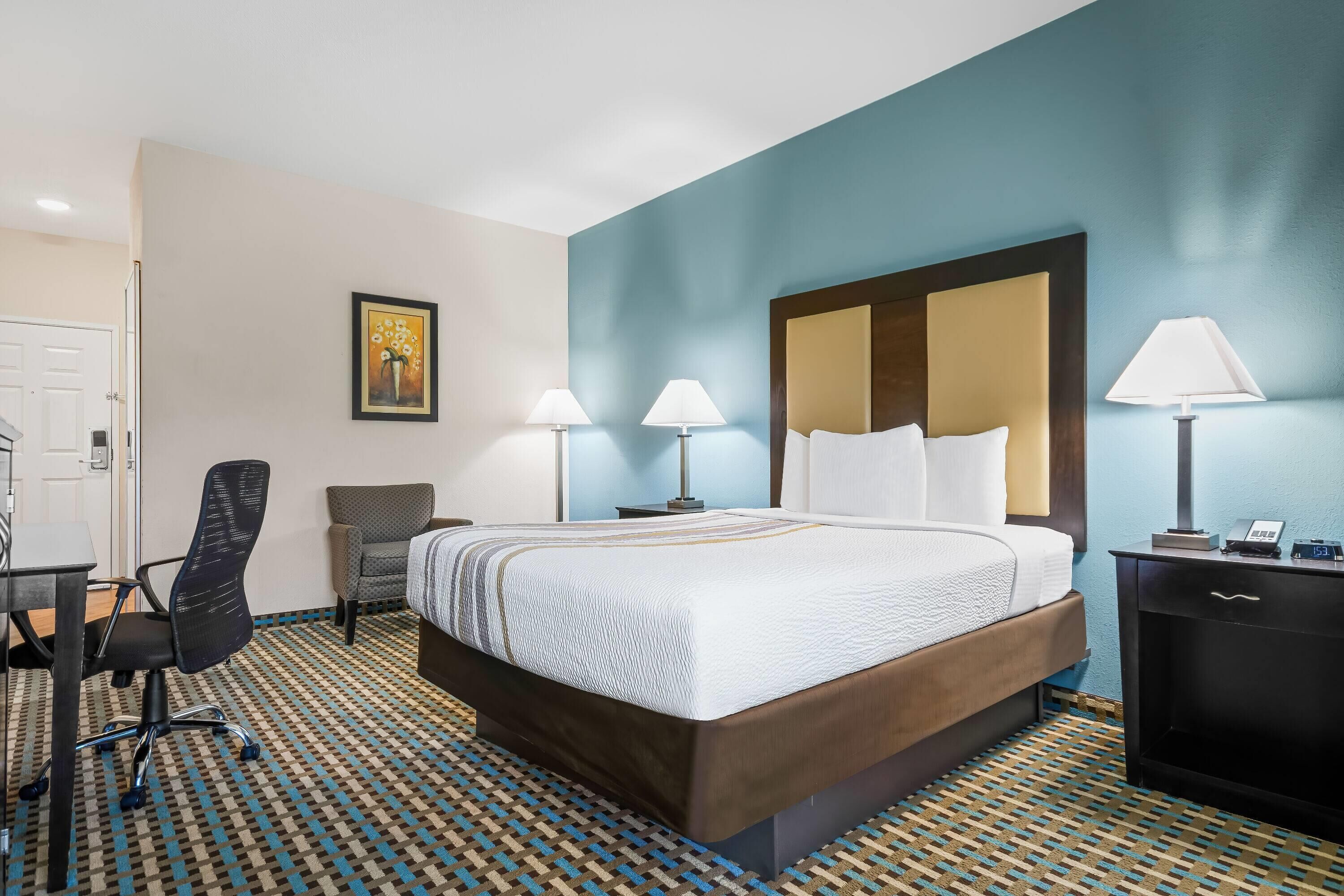 A hotel room with a bed, desk, chair, and two lamps.
