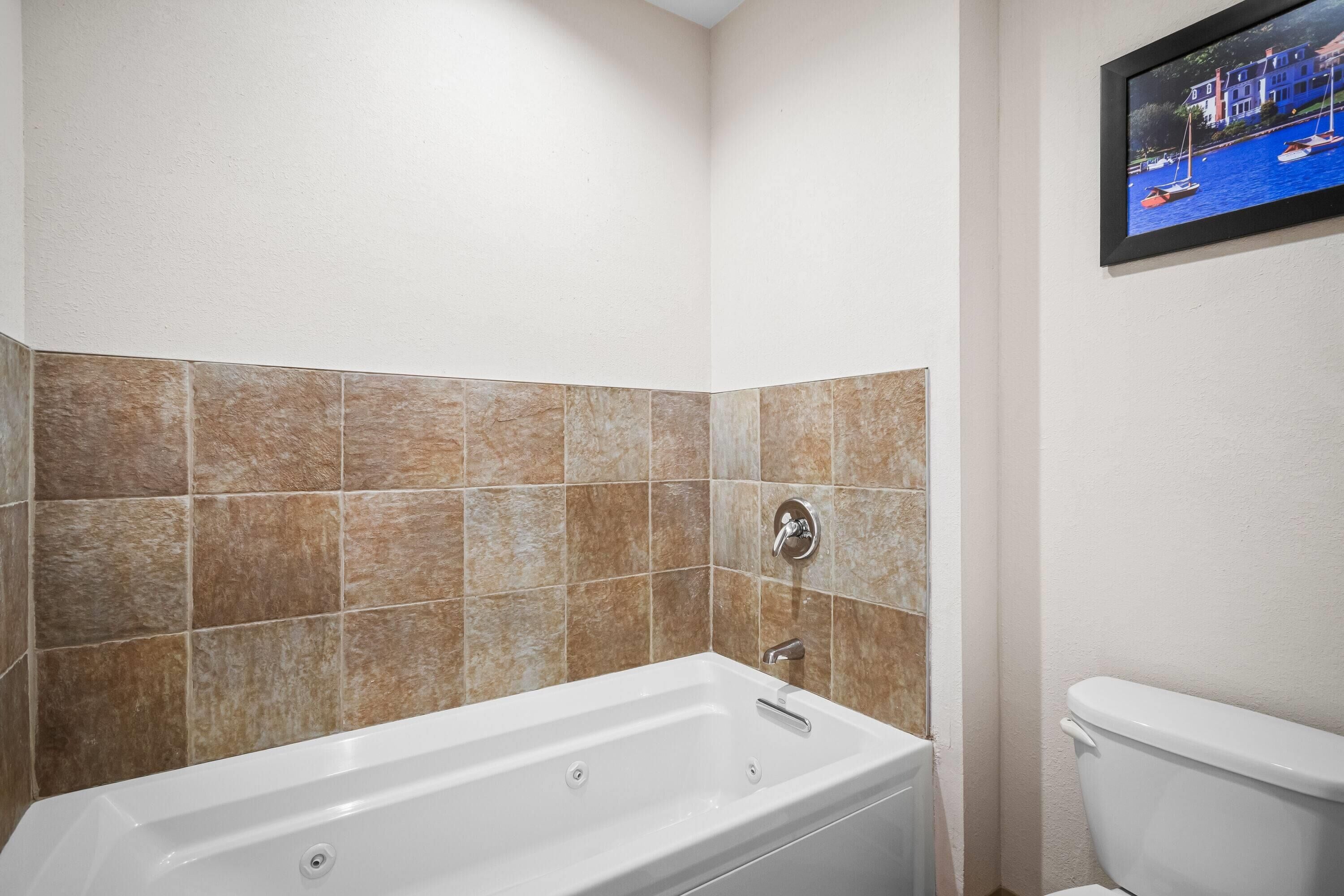 A bathroom with a bathtub, a toilet, and a tiled wall.