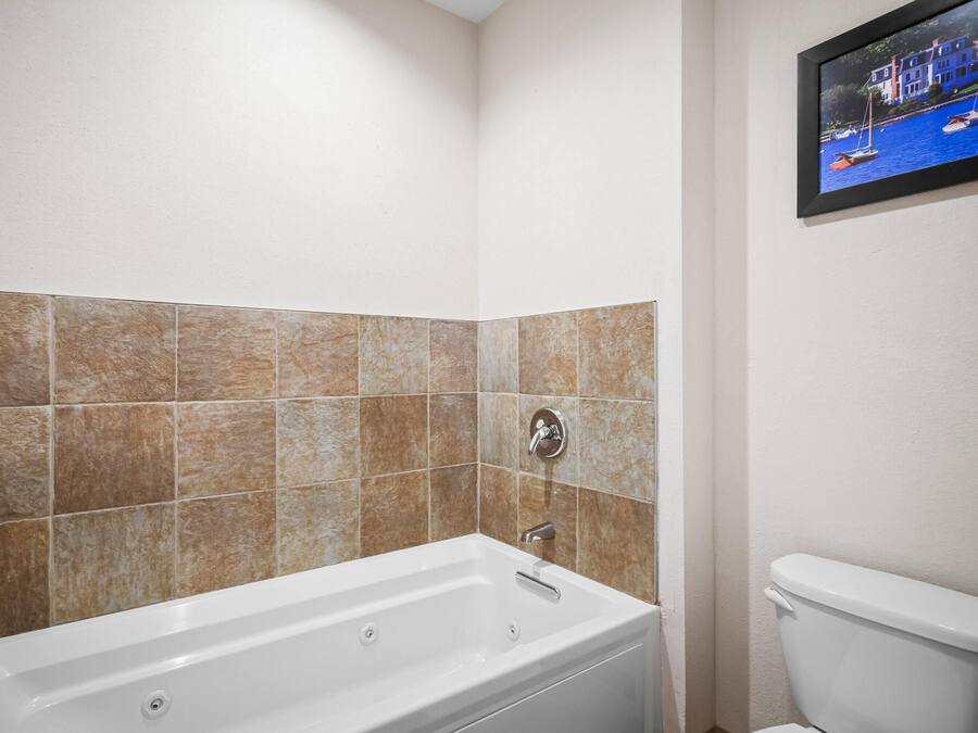 A bathroom with a bathtub, a toilet, and a tiled wall.