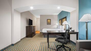 Habitación de hotel con cama, escritorio, silla, lámpara, televisión y alfombra estampada.
