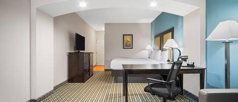 A hotel room with a bed, desk, chair, lamp, TV, and patterned carpet.