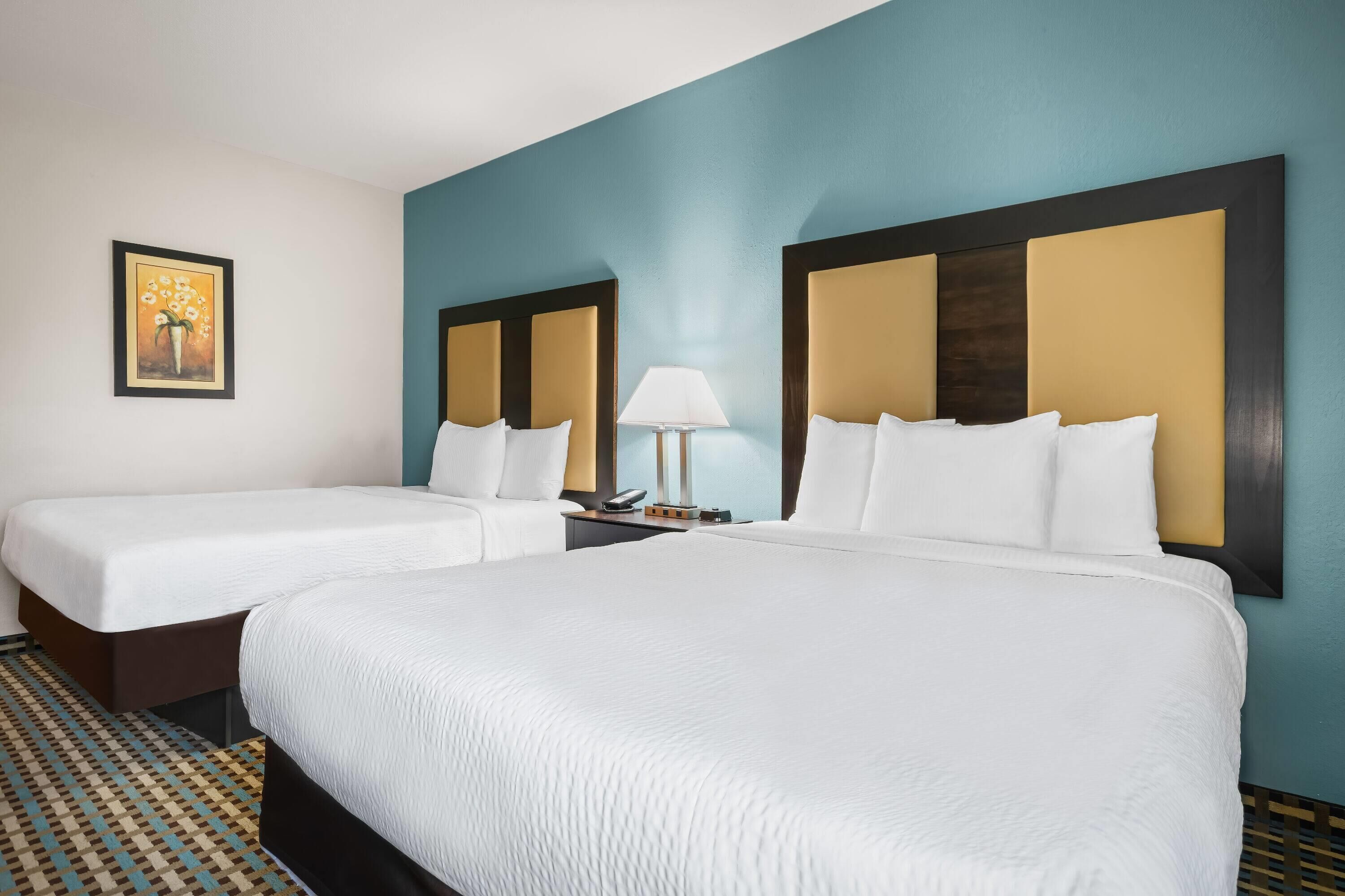 Habitación de hotel con dos camas, una mesita de noche con lámpara y un cuadro enmarcado en la pared.