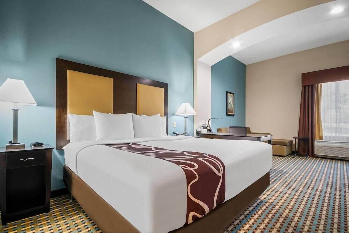 A hotel room with a large bed, bedside tables, a desk, and a window with curtains.