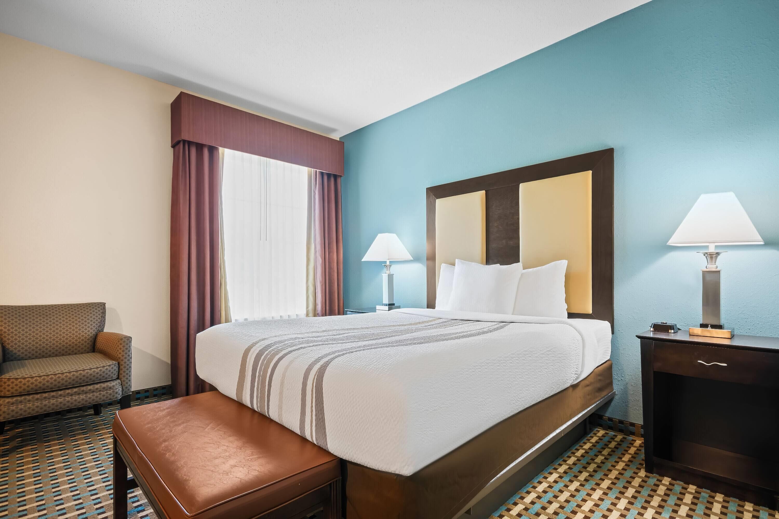 A hotel room with a large bed, a bedside table with a lamp, a chair, and a patterned floor.