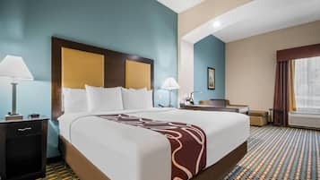 Quarto de hotel com uma cama grande, uma escrivaninha, uma cadeira, um abajur e uma janela com cortinas.