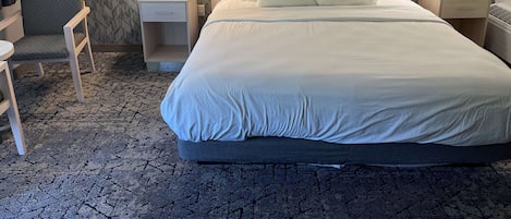 Une chambre d’hôtel avec un grand lit, deux tables de chevet avec des lampes, une chaise, une petite table et un tableau encadré au mur.