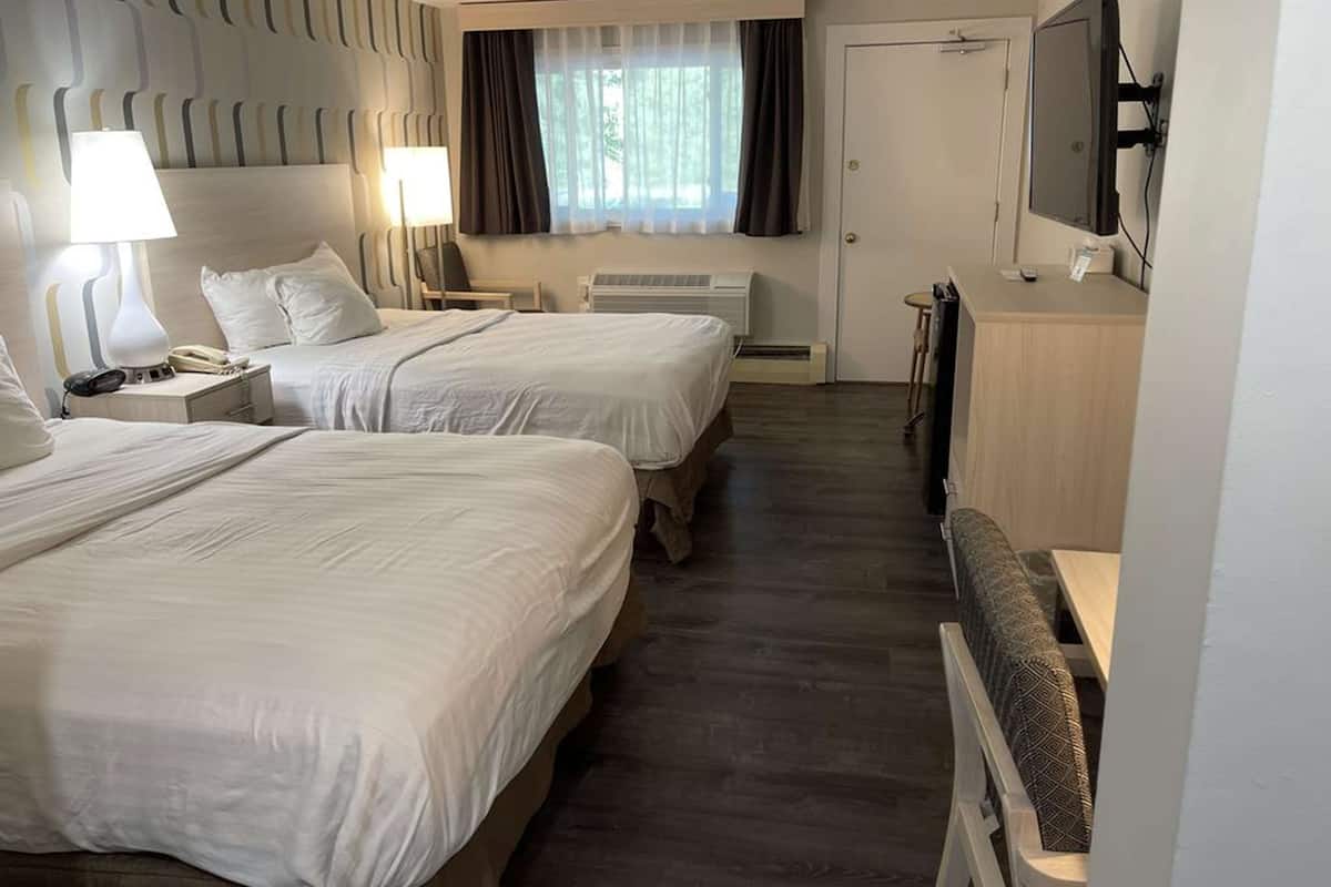 A hotel room with two beds, a desk with a chair, a TV, and a window with curtains.