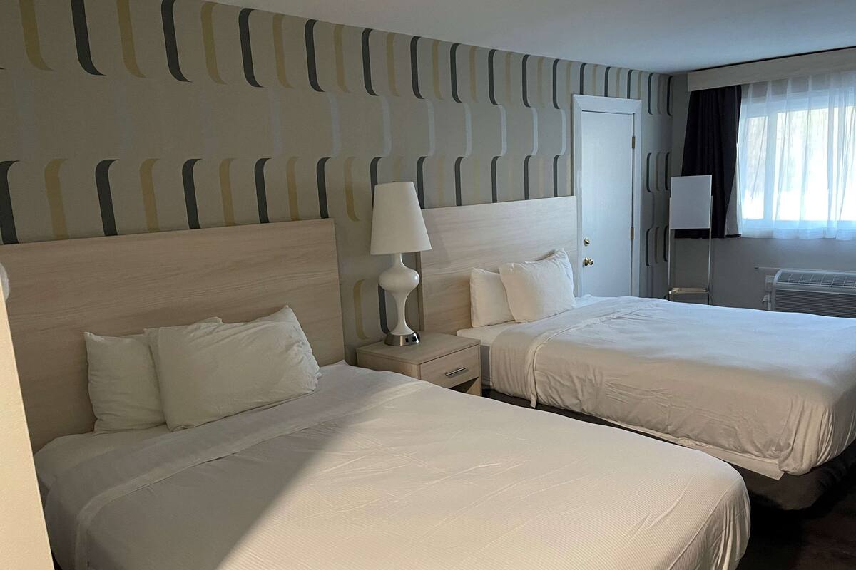 A hotel room with two beds, a nightstand with a lamp, a dresser, and a window with curtains.