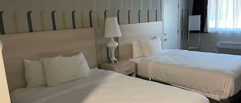 A hotel room with two beds, a nightstand with a lamp, a dresser, and a window with curtains.