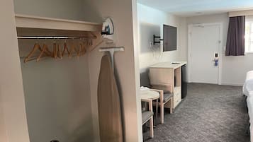 A hotel room with a bed, a desk with a chair, a TV, and a coat rack with hangers.