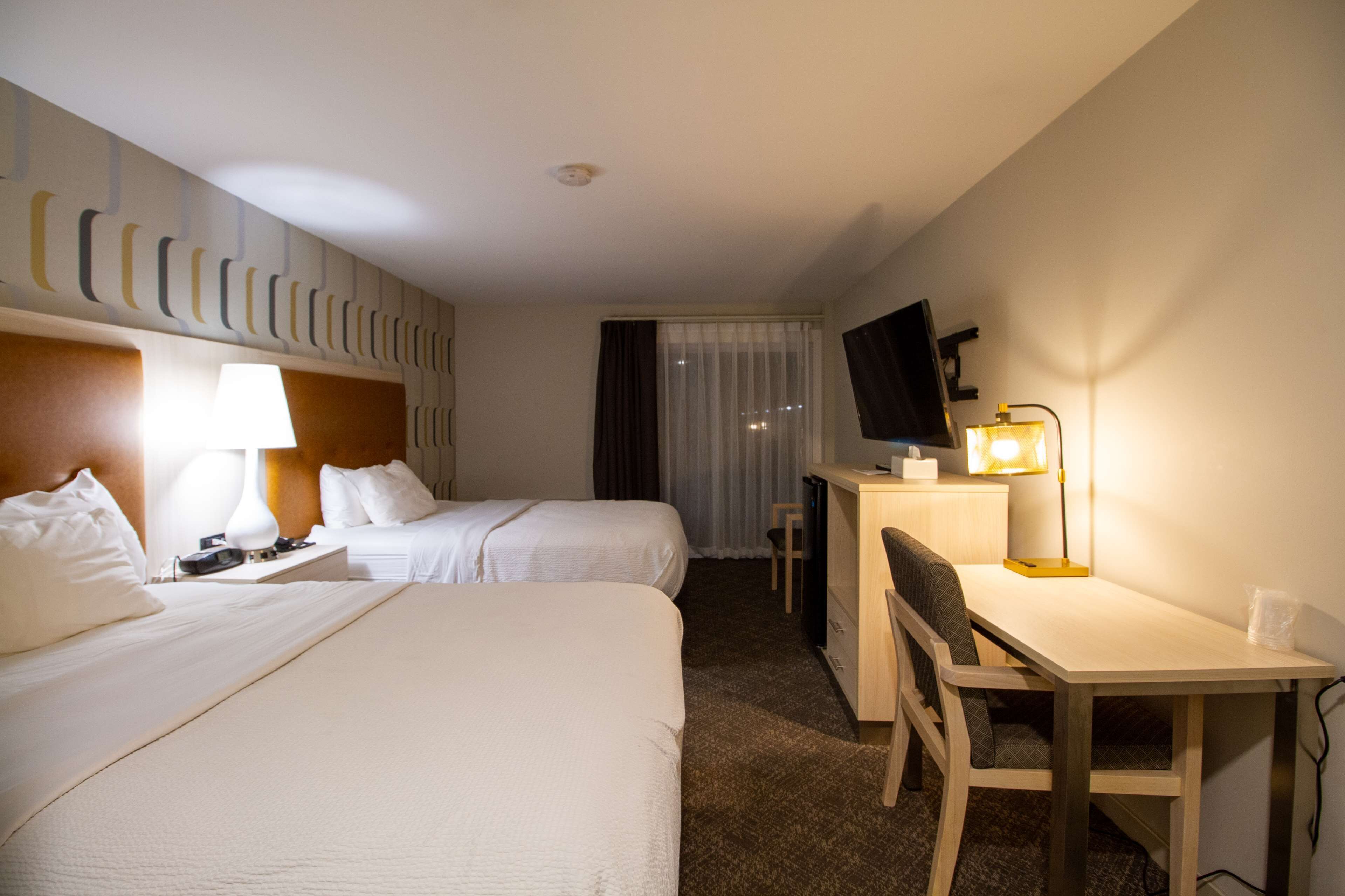 Ein Hotelzimmer mit zwei Betten, einem Schreibtisch, einem Stuhl, einem Fernseher und einer Lampe.