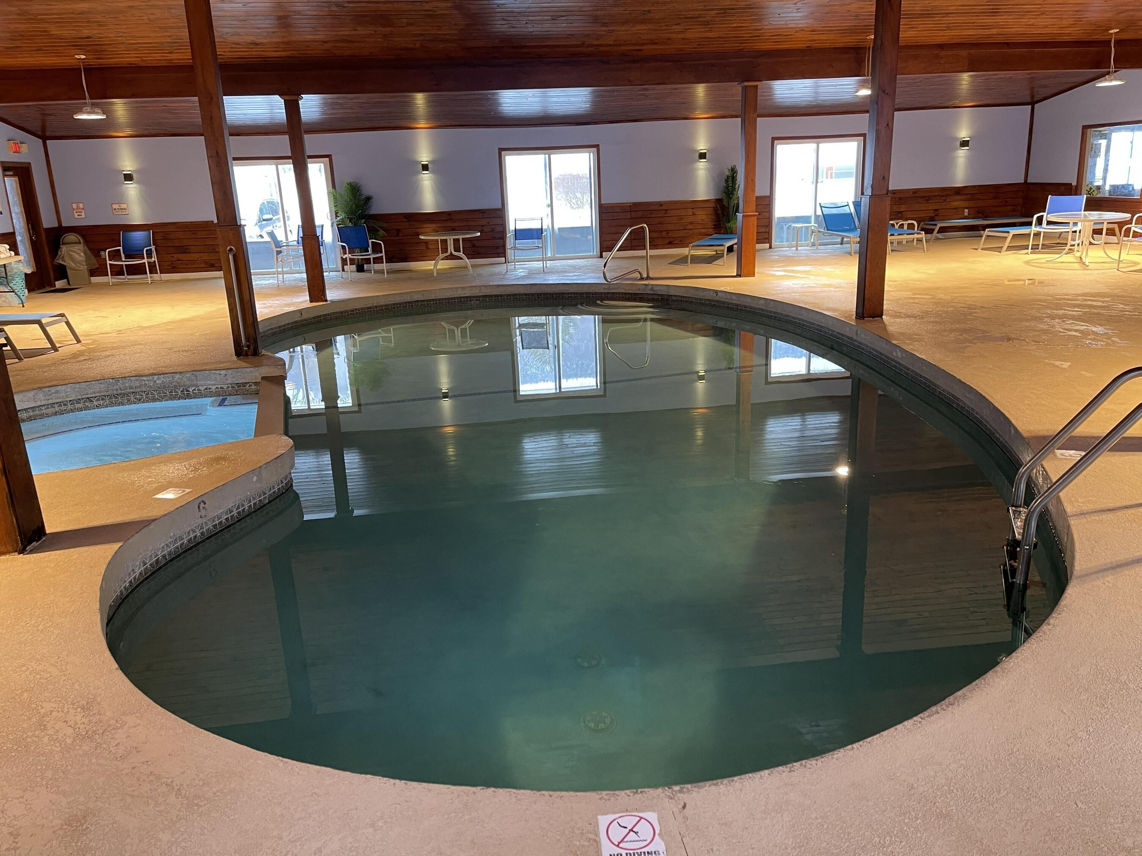 An indoor swimming pool with a wooden ceiling, clear glass walls, and a no diving sign.
