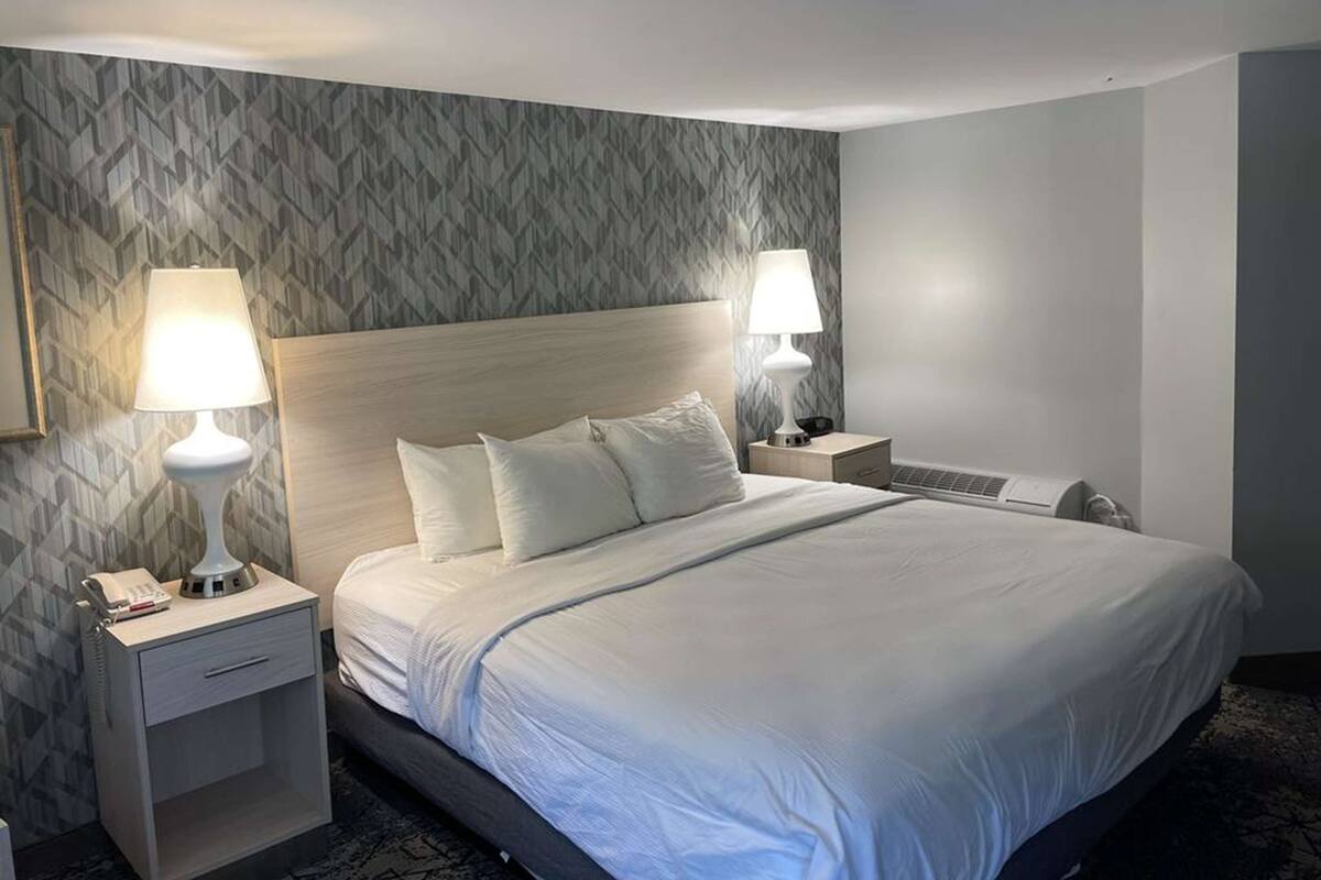 A hotel room with a large bed, two bedside tables, a nightstand, and a wall-mounted telephone.