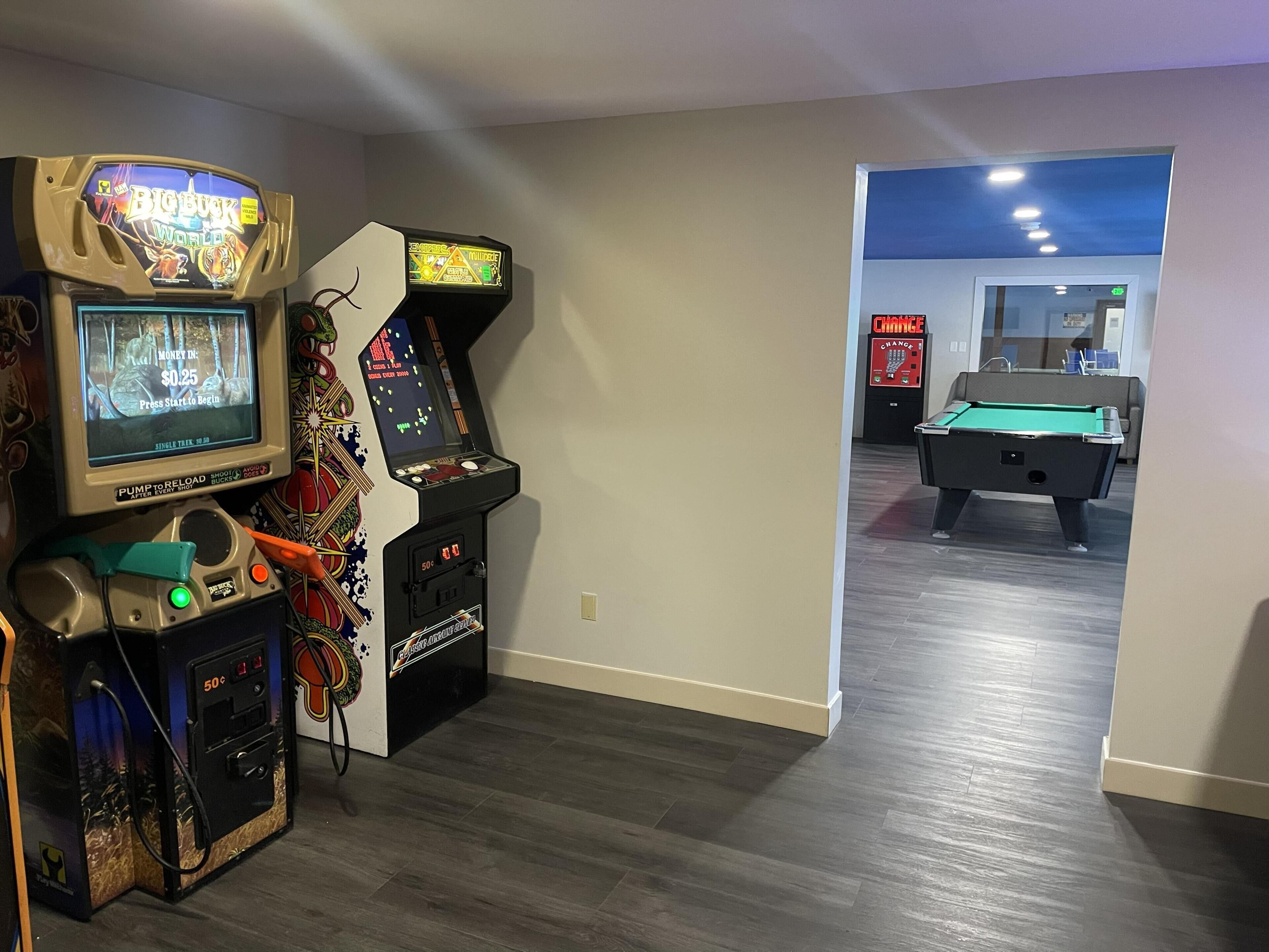 A room with a pool table, arcade games, and a billiards table.