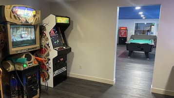 A room with a pool table, arcade games, and a billiards table.