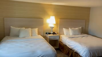 A hotel room with two beds, each with white bedding and pillows. There is a nightstand between the beds with a lamp, phone, and keys.