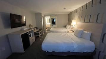 A hotel room with two beds, a desk, a TV, and a bathroom visible through an open door.