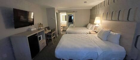 A hotel room with two beds, a desk, a TV, and a bathroom visible through an open door.