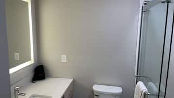 Un baño moderno con un espejo grande, un lavamanos, un inodoro y una ducha con cerramiento de vidrio.