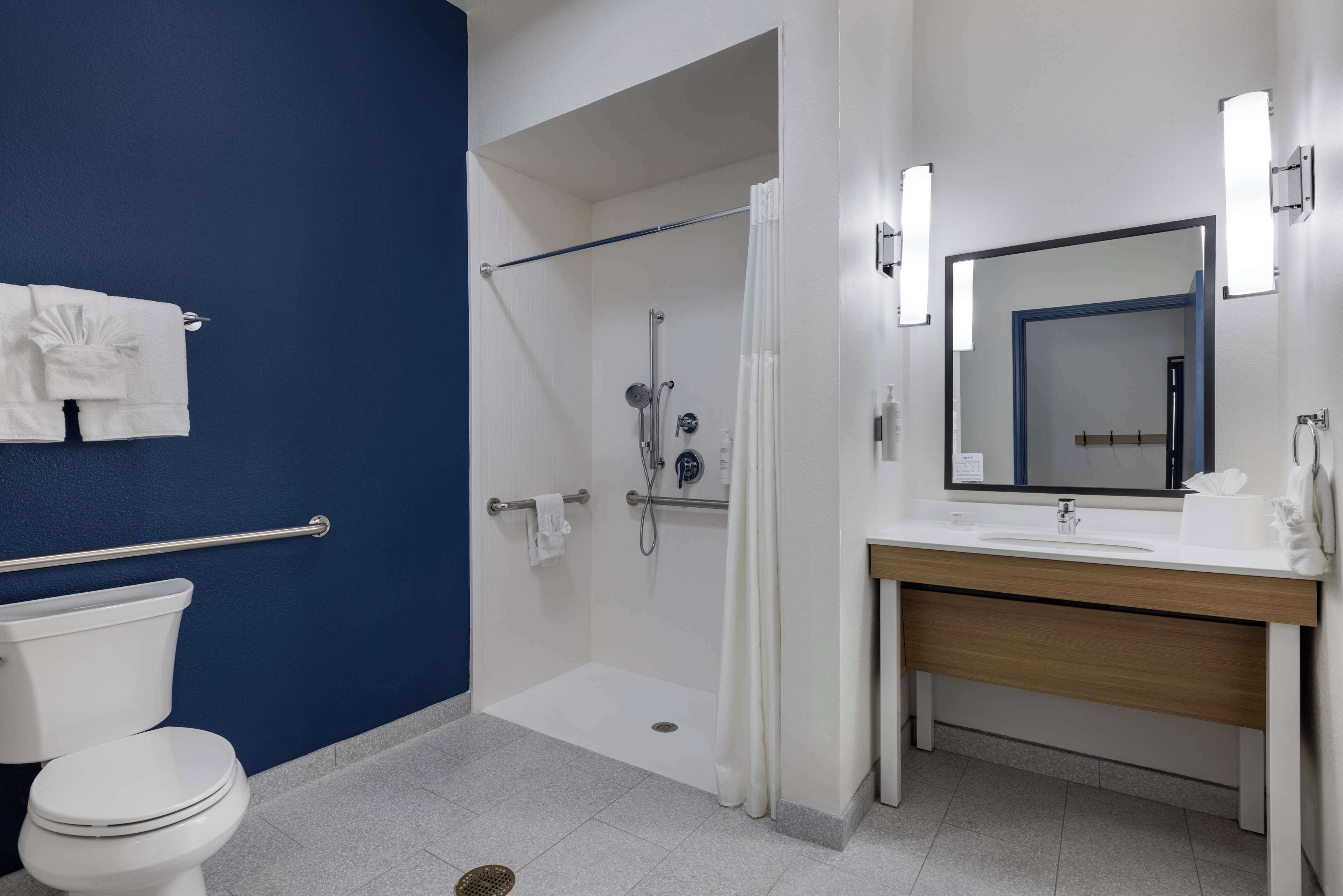 A bathroom with a blue wall, a white toilet, a shower with a glass door, a wooden vanity with a mirror, and a towel rack.
