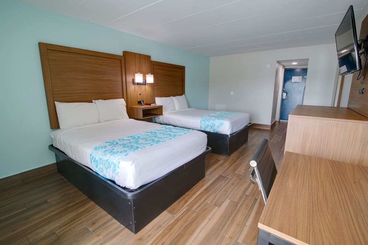 A hotel room with two beds, wooden headboards, a desk, and a TV.