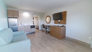 A modern apartment with a kitchenette, a dining area, a living room with a sofa, and a TV mounted on the wall. - Seashire Inn & Suites (Virginia Beach)