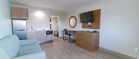 A modern apartment with a kitchenette, a dining area, a living room with a sofa, and a TV mounted on the wall.