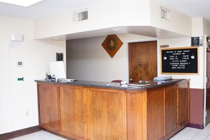 Mostrador de recepción con detalles de madera, una pantalla digital y un cartel con horarios de registro y política de mascotas.
