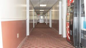 Ein Hotelkorridor mit gemustertem Teppich, weißen Wänden und einer Coca-Cola-Getränkeautomaten.