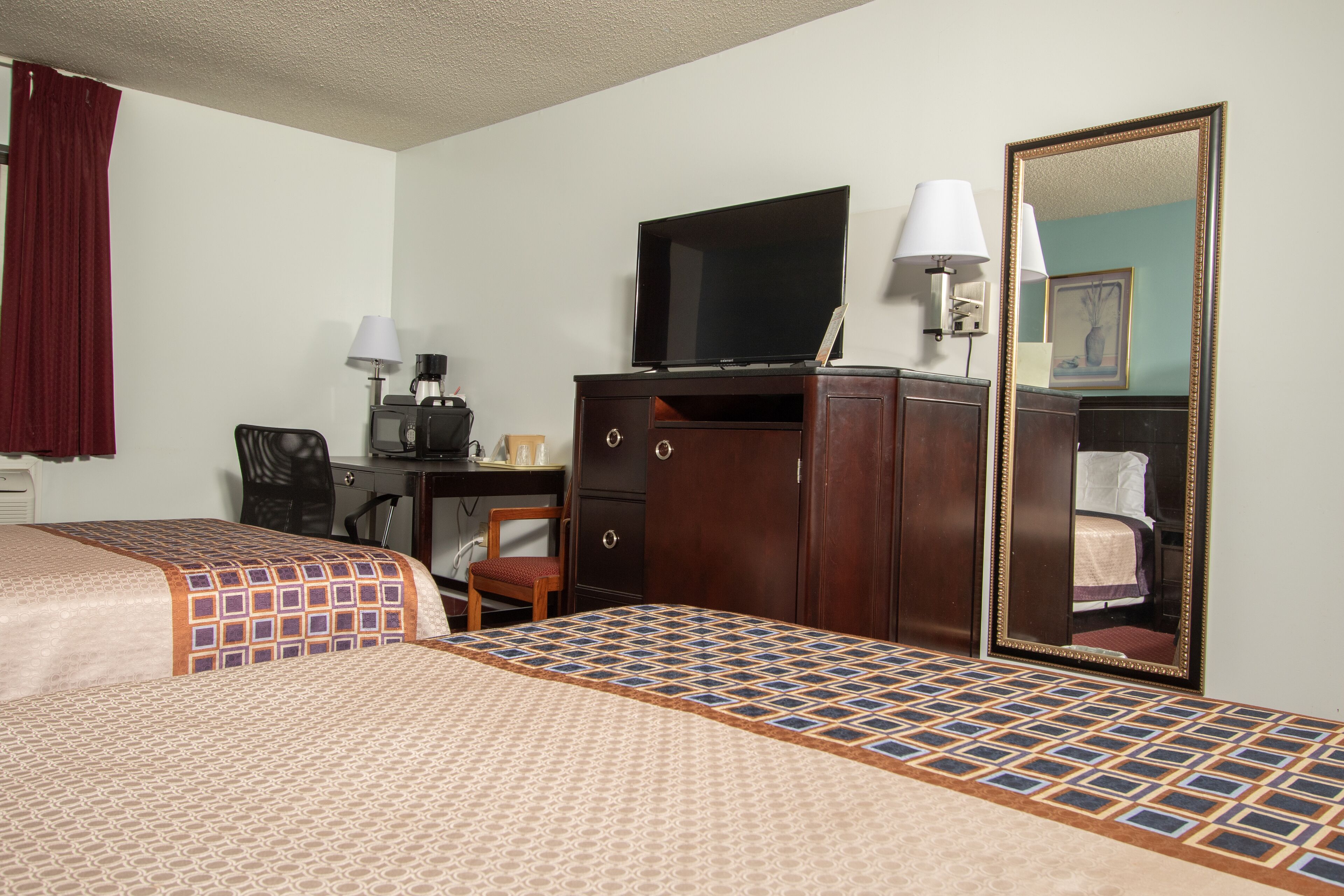 A hotel room with two beds, a desk with a television, a dresser, and a mirror.