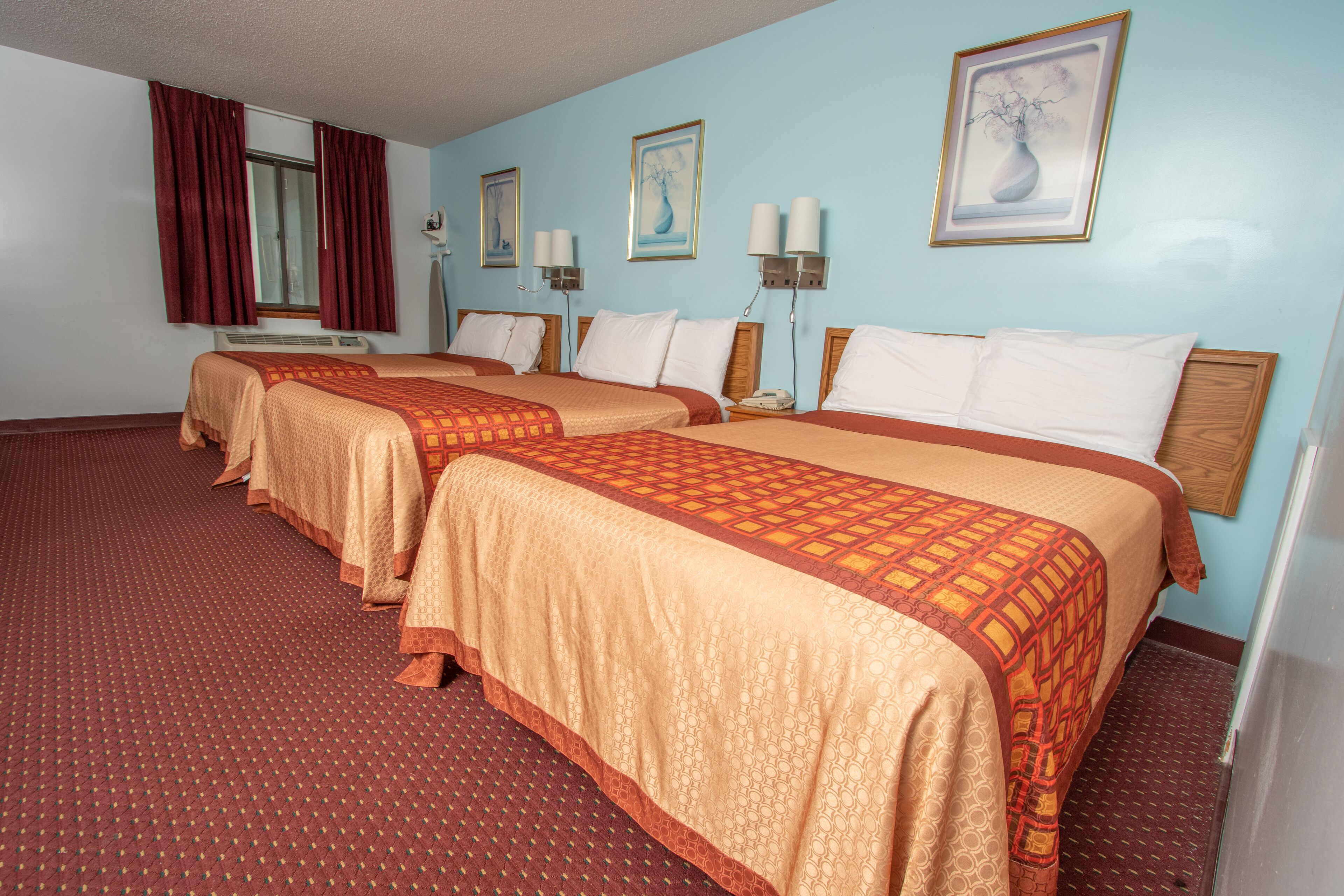 A hotel room with two beds, red carpet, and wall-mounted lamps.