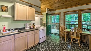 A kitchen with wooden cabinets, a stove, and a dining area with a table and chairs. - Nantahala Cabins (Bryson City)
