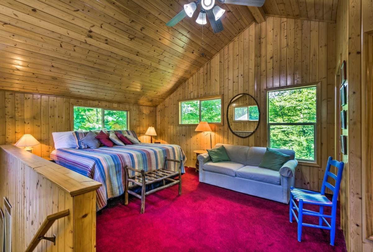 A cozy cabin room with a bed, a sofa, a chair, and a red carpet.