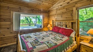 A wooden cabin bedroom with a bed, a window, a ceiling fan, and a view of the outdoors. - Nantahala Cabins (Bryson City)
