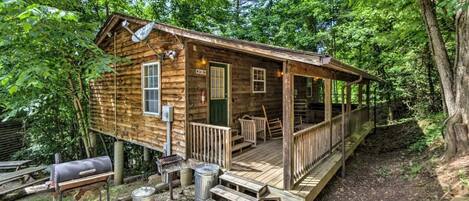 A rustic cabin with a wooden deck, a porch, and a grill outside.
