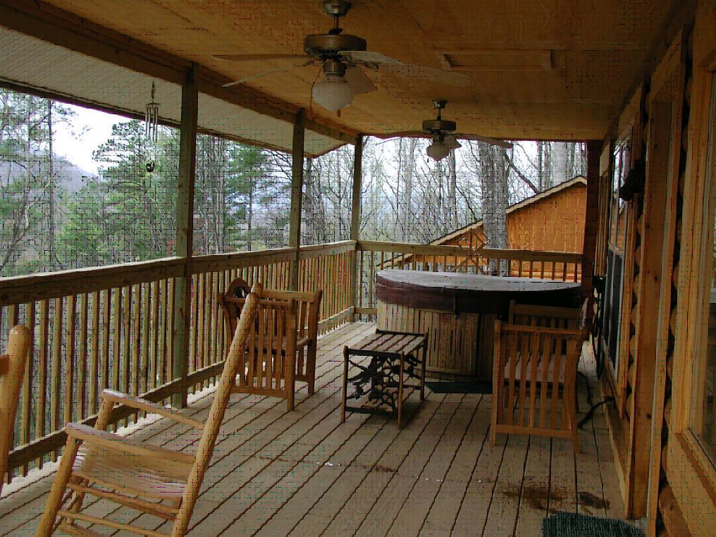 A wooden deck with a table and chairs, a ceiling fan, and a view of the forest.