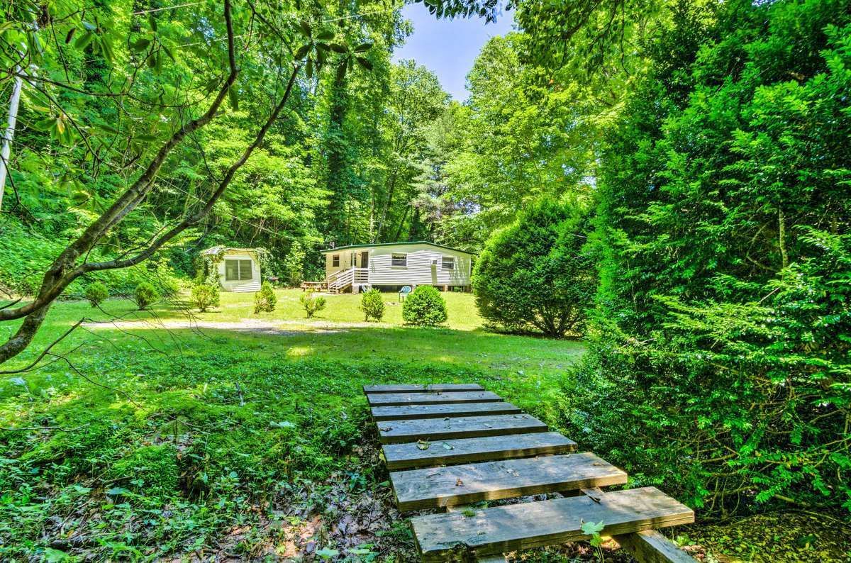 A rustic cabin surrounded by dense forest, with a wooden staircase leading to the entrance.