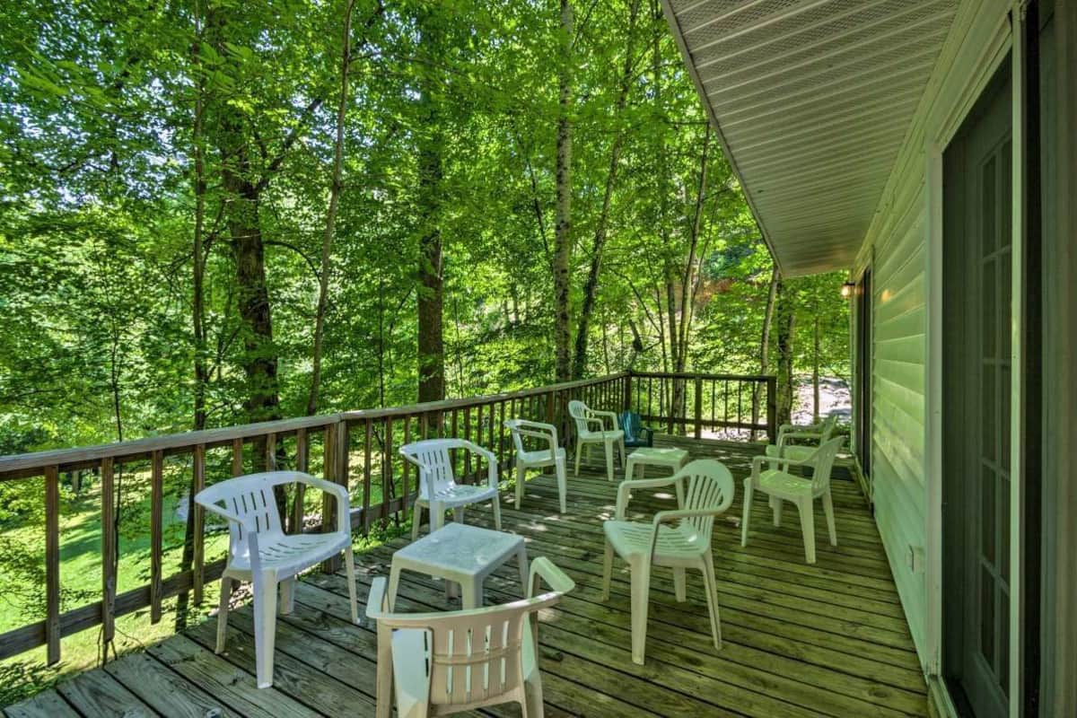 A covered outdoor deck with wooden railings, surrounded by lush green trees.