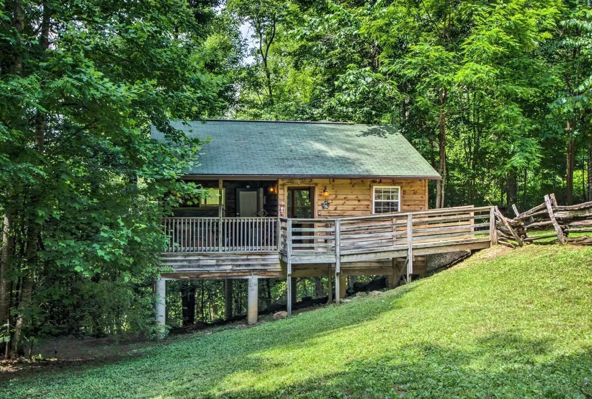 A wooden cabin with a balcony, surrounded by lush greenery.