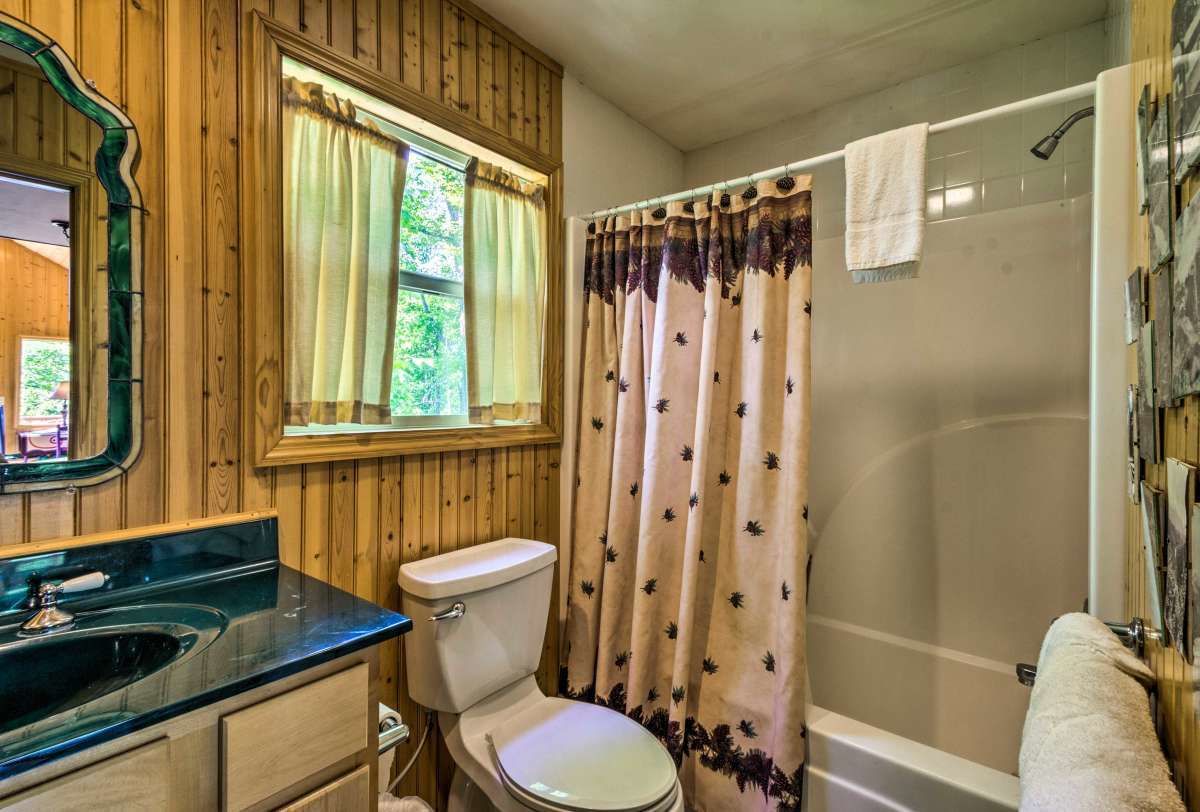 A bathroom with a wooden vanity, a toilet, a bathtub, and a window with curtains.